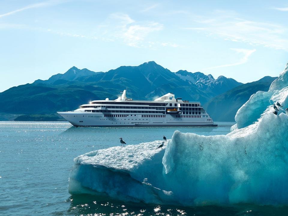 An expedition ship sailing past a glacier ice floe with seagulls, mountains beyond, Alaska